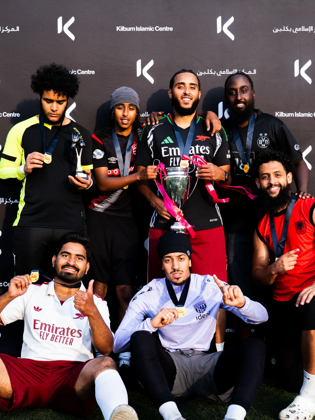 The winning team with the trophy, in front of a Kilburn Islamic Centre backdrop