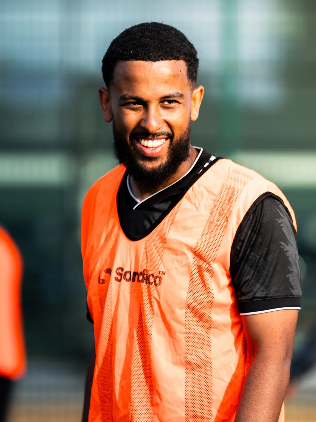 A player in an orange bib, smiling
